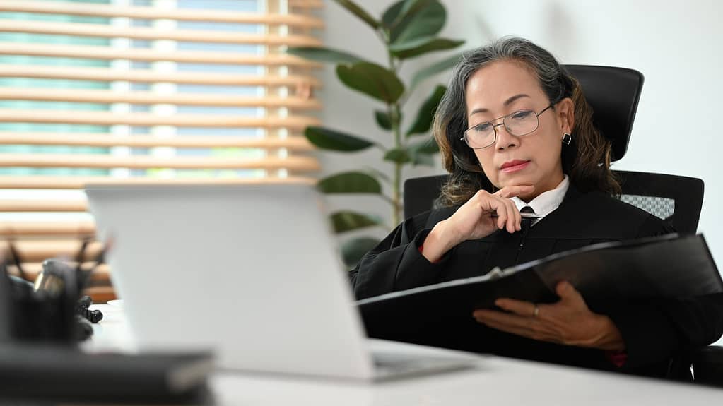 Focused mature female lawyer in judge uniform working with documents at office.