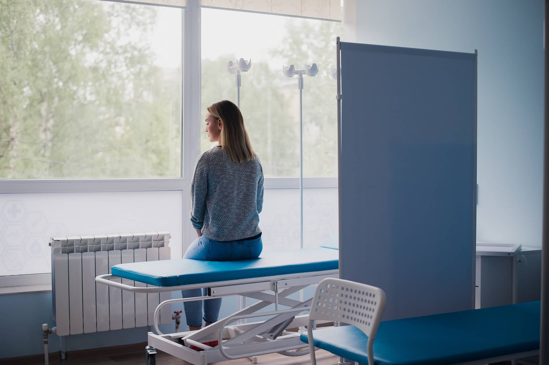 Young pregnant woman sitting on bed in comfortable ward, waiting for doctor thoughtfully