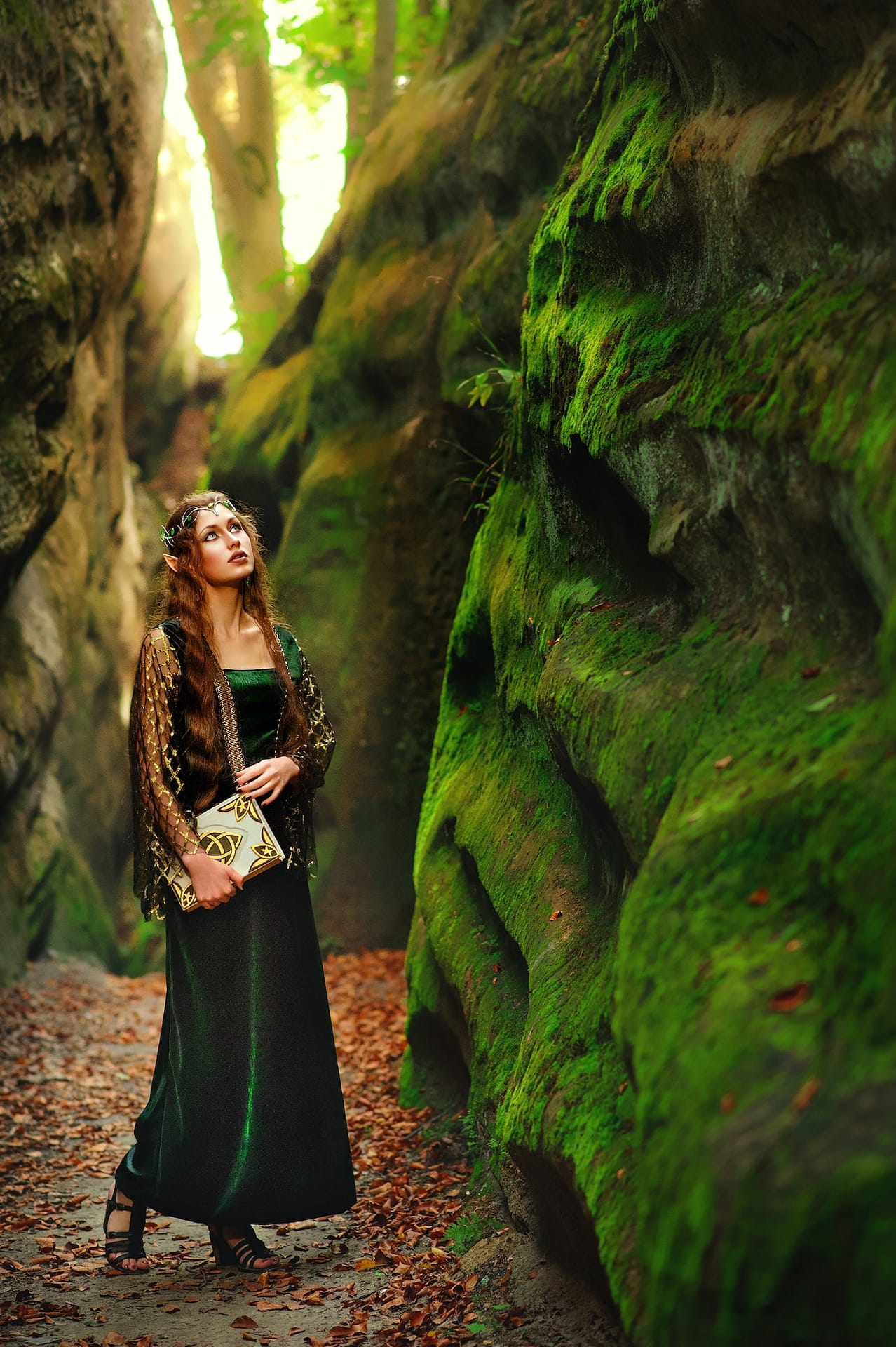 Young female elf wandering in the forest holding an old book